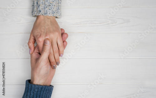 Man's hand holds a woman's hand on a white wooden background. The concept of love, trust and support in a relationship. Copy space. Top view. Flatlay composition.
