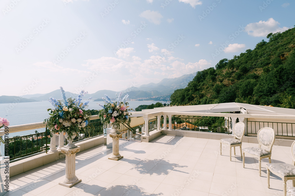 Bouquets of flowers in front of antique chairs stand on a terrace overlooking the sea and mountains