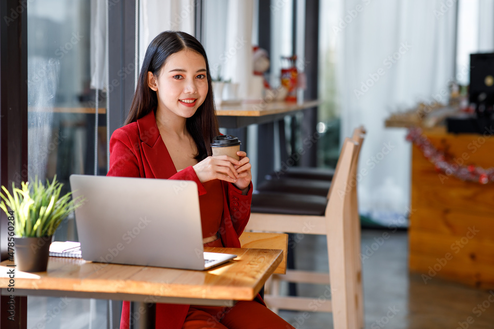 Asian Young businesswoman wearing red suit using a laptop computer. Female working on laptop in an in the cafe. Asian Young businesswoman wearing red suit using a laptop computer. Female working on laptop in an in the cafe.