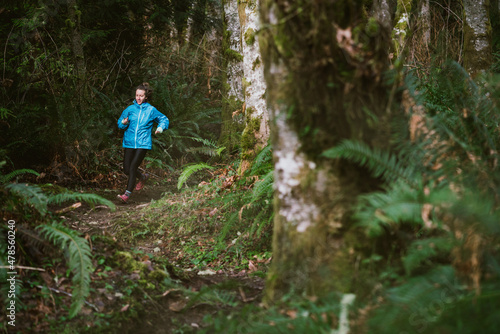 Female trail runner runs on rocky trail in forest surrounded by ferns photo