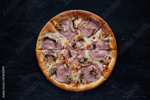 Pizza with cheese, ham, bacon and mushrooms on a black stone background. Top view