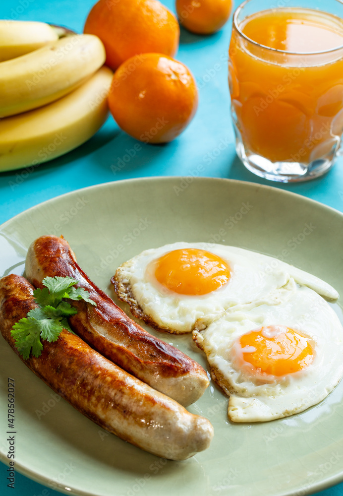 A Morning Breakfast wit two German Sausages, Two Eggs, an Orange Juice and some Fruit.