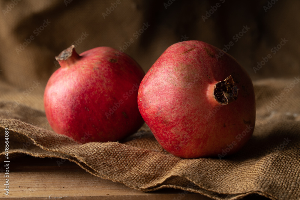 Two ripe juicy pomegranates on gray burlap. Food background.