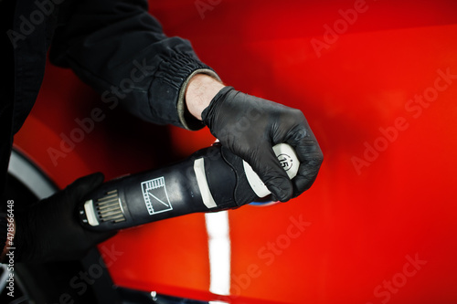 Car detailing concept. Hands of man with orbital polisher in repair shop polishing orange suv car. © AS Photo Family