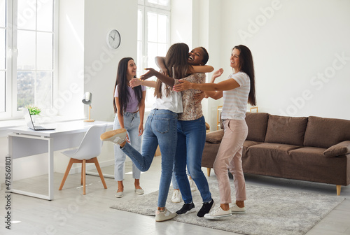 Diverse mixed race group of happy excited beautiful young women hugging their friend as they meet her at a casual get together, friendly gathering or cozy party at home. Female friendship concept