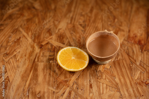 Mezcal jicara next to an orange red in a wooden table photo