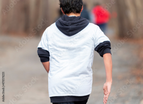 Back of a boy running up a small hill in the woods with a blurred background