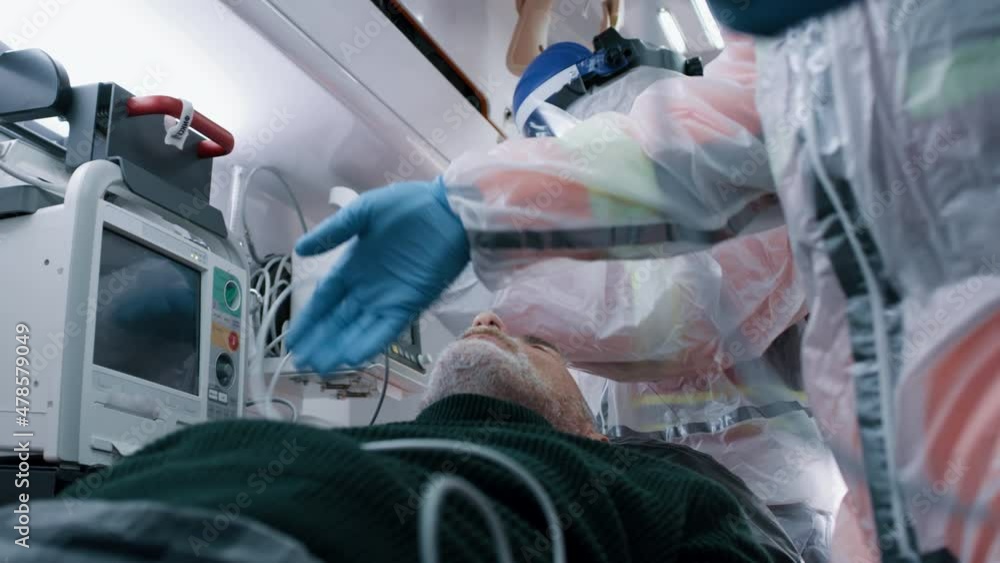 Low angle of doctors in hazmat suits putting pulse oximeter on finger of elderly patient while working in emergency medicine vehicle during pandemic Low angle of doctors in hazmat suits putting pulse oximeter on finger of elderly patient while working in emergency medicine vehicle during pandemic