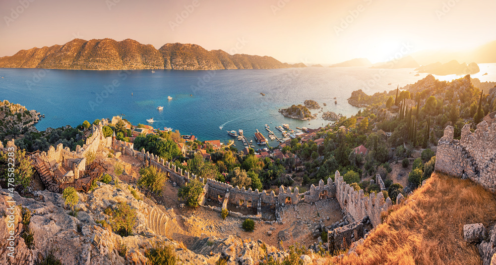 Naklejka premium Famous Simena ancient castle on a top of a hill with stunning panoramic view over the sea at sunset time. Travel and tourist attractions at Kekova island, Turkey.