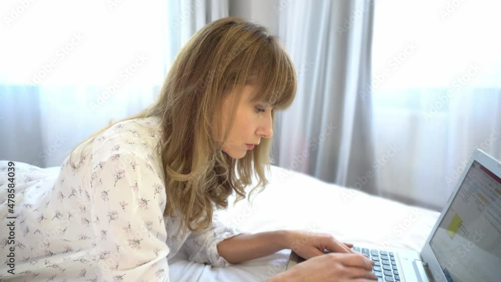 Work at home. Quarantine. The woman is working on laptop at home. The woman lies on the bed and works on a laptop. Remote work. Work at home. Quarantine. The woman is working on laptop at home. The woman lies on the bed and works on a laptop. Remote work.