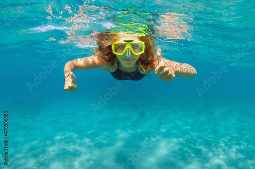 Young girl in snorkeling mask dive in coral reef sea lagoon to explore underwater world. Family travel lifestyle in summer adventure camp. Swimming activities on beach vacation with kids.