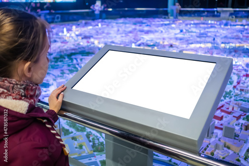 Woman looking at blank digital interactive white display kiosk at exhibition or museum with futuristic sci-fi interior. Mock up, copyspace, template, white screen, technology concept