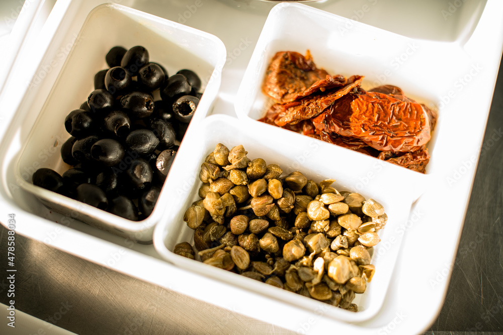 view of white trays with black olives and sun-dried tomatoes and green grains view of white trays with black olives and sun-dried tomatoes and green grains
