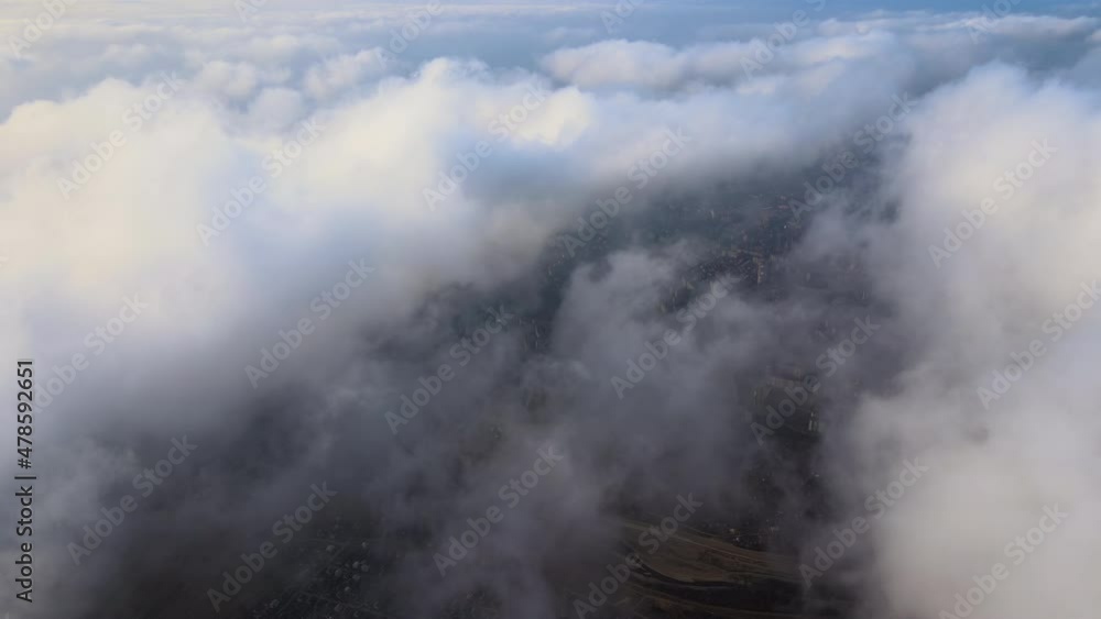 Aerial view from high altitude of distant city covered with puffy cumulus clouds flying by before rainstorm. Airplane point of view of landscape in cloudy weather Aerial view from high altitude of distant city covered with puffy cumulus clouds flying by before rainstorm. Airplane point of view of landscape in cloudy weather