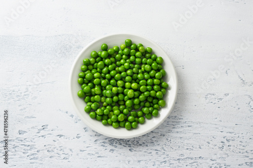 White plate with steamed green peas on a light blue background. Healthy delicious dietary ingredient for cooking