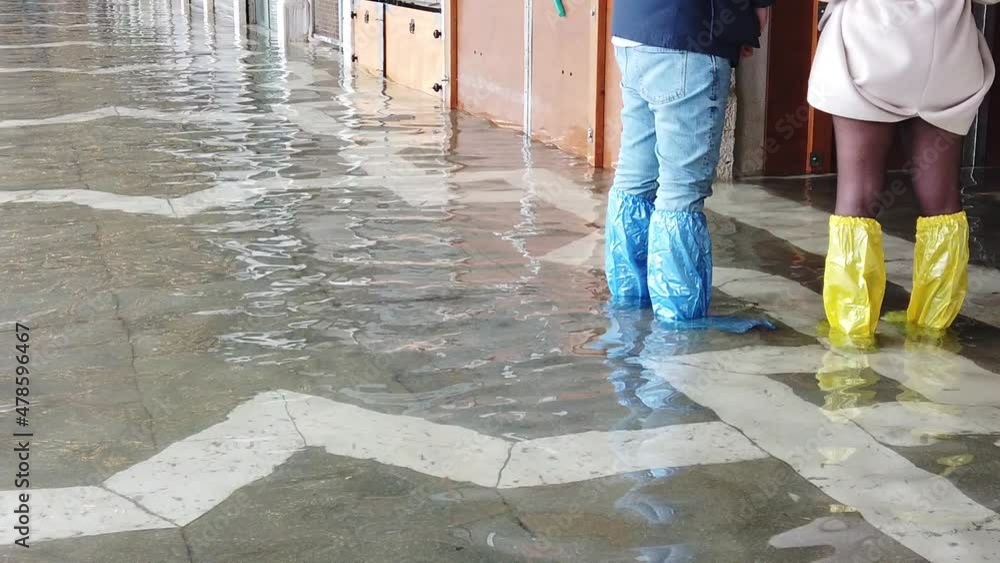 Venice, Italy - January 2022 - San Marco square submerged by high water on a sunny day while tourists are having fun with colored boots Venice, Italy - January 2022 - San Marco square submerged by high water on a sunny day while tourists are having fun with colored boots