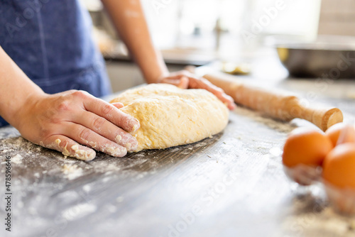 Female hands making dough for baking on wooden table near rolling pin, eggs and milk bottle. Culinary, cooking, baking concept