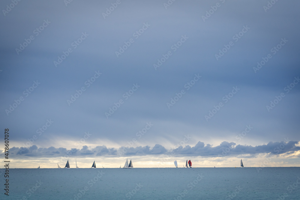 une régate de voiliers au loin sur l'horizon , sous un ciel hivernal et nuageux
