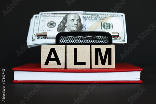 wooden blocks with dollar bills on a black background with text ALM conceptual symbol.