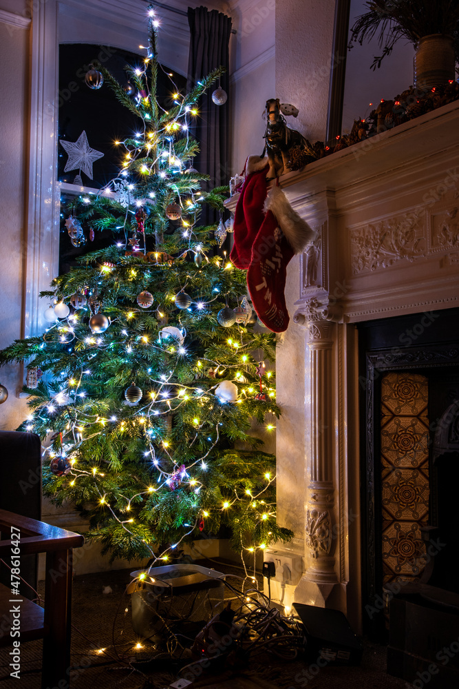 Christmass tree in the old house by the unlit fire place with some decorations and lights