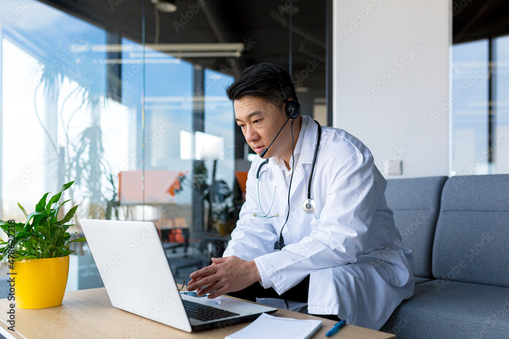 Asian doctor consults online patient video call, man uses laptop and headset Asian doctor consults online patient video call, man uses laptop and headset