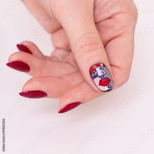 Beautiful female hand with creative manicure nails, red gel polish, lips design, white background