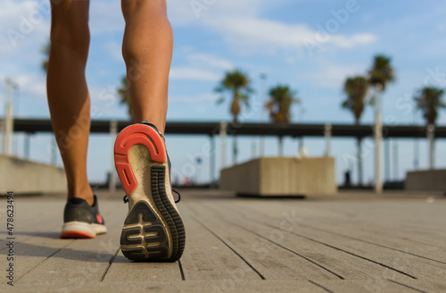 shot of legs of a woman with sport shoes who is about to run from a place with unfocused palm trees in the background in a sunny day