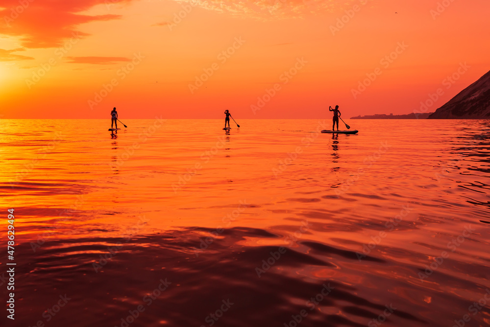 Travelers on stand up paddle board at quiet sea with sunset or sunrise. Girls on Red Paddle sup board and sunset