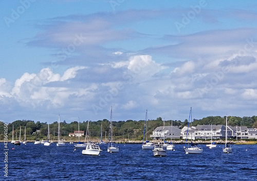 Sailboats docked in a marina in Bristol Harbor, Rhode Island, on a sunny afternoon with a few cumulus clouds