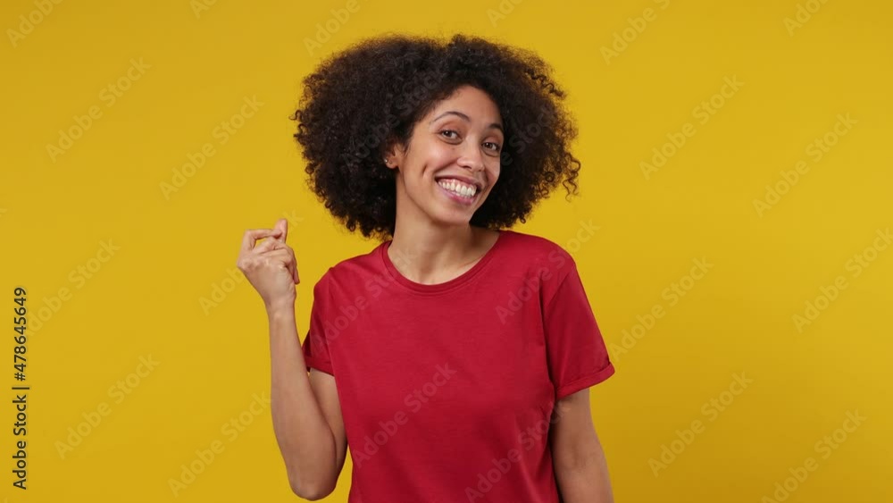 Happy young black woman 20s wears red t-shirt dance waving rising expressive gesticulating hands have fun enjoy snaps her fingers to music rhythm isolated on plain yellow background studio portrait Happy young black woman 20s wears red t-shirt dance waving rising expressive gesticulating hands have fun enjoy snaps her fingers to music rhythm isolated on plain yellow background studio portrait