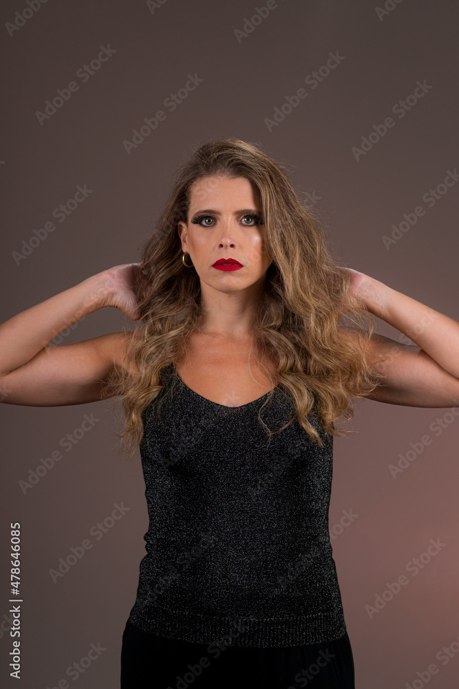 Retrato de mulher loira de olhos verdes, cabelo cacheado em fundo cor salmão no estúdio. Jovem olhando para a câmera com as mãos no cabelo e séria. Retrato de mulher loira de olhos verdes, cabelo cacheado em fundo cor salmão no estúdio. Jovem olhando para a câmera com as mãos no cabelo e séria.
