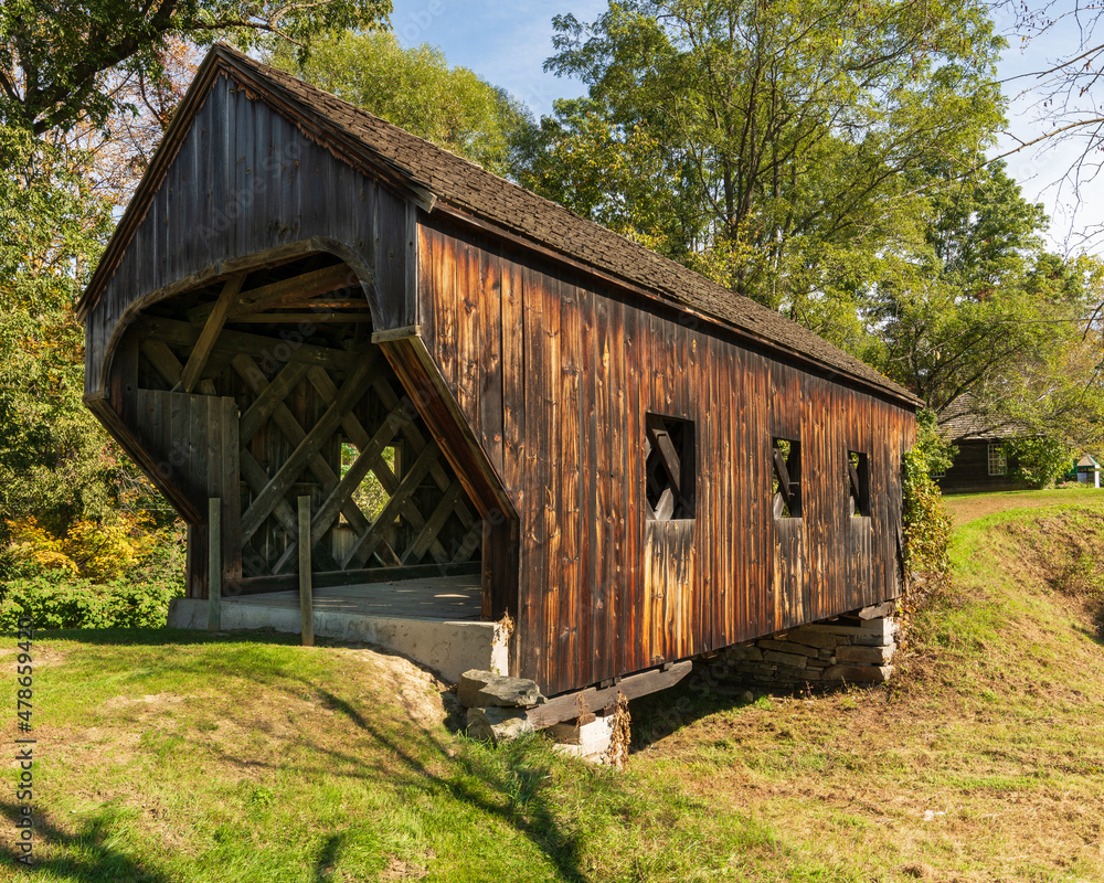 Side view of the Baltimore covered bridge is an old wooden bridge located in Springfield Vermont with dark weathered wood located next to the Eureka one-room schoolhouse. Summer day in full sun. Side view of the Baltimore covered bridge is an old wooden bridge located in Springfield Vermont with dark weathered wood located next to the Eureka one-room schoolhouse. Summer day in full sun.
