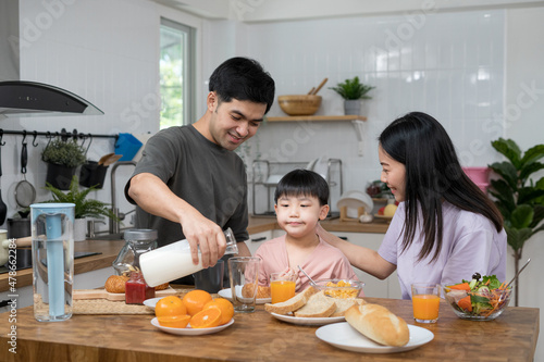 Asian family breakfast at home. Parents and children enjoy eating together, talking with laughter and good atmosphere. Father and mother plays with son playfully at kitchen table.