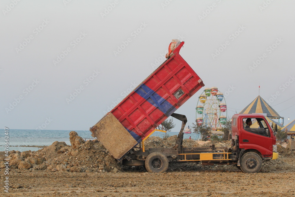 Obraz premium The red truck is unloading its cargo on the beach