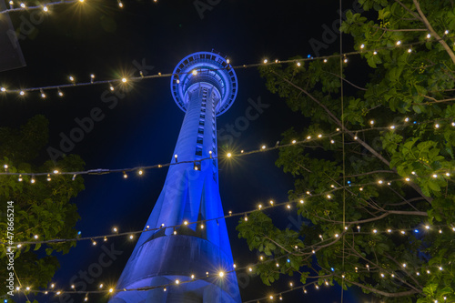 Fotografie Night scene tall circular tower illuminated blue viewed through strings of decorative fairy lights