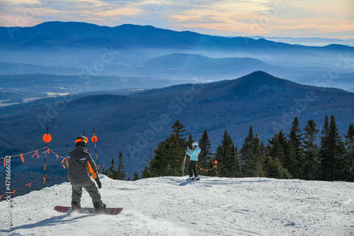 Snowboarder and skier standing on a top of Peak Mansfield Summit at Stowe Vermont Mountain Resort. Beautiful winter day.
