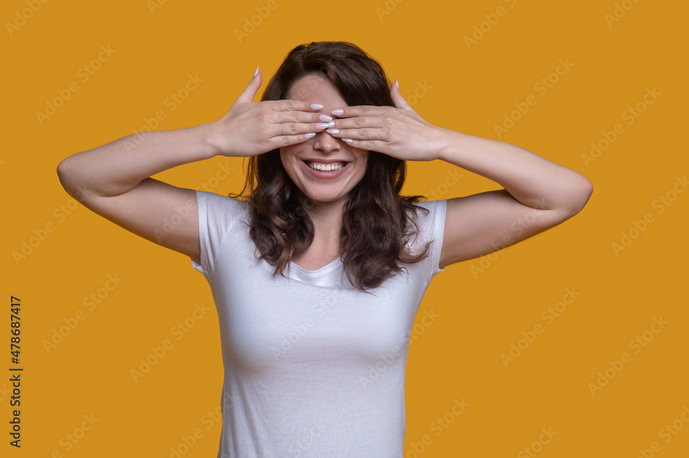 Cheerful female dressed in casual clothes hiding her face