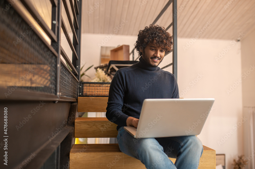 Man looking at laptop screen sitting on stairs Man looking at laptop screen sitting on stairs