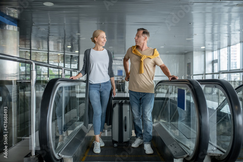 Two middle-aged airport passengers getting off the moving staircase