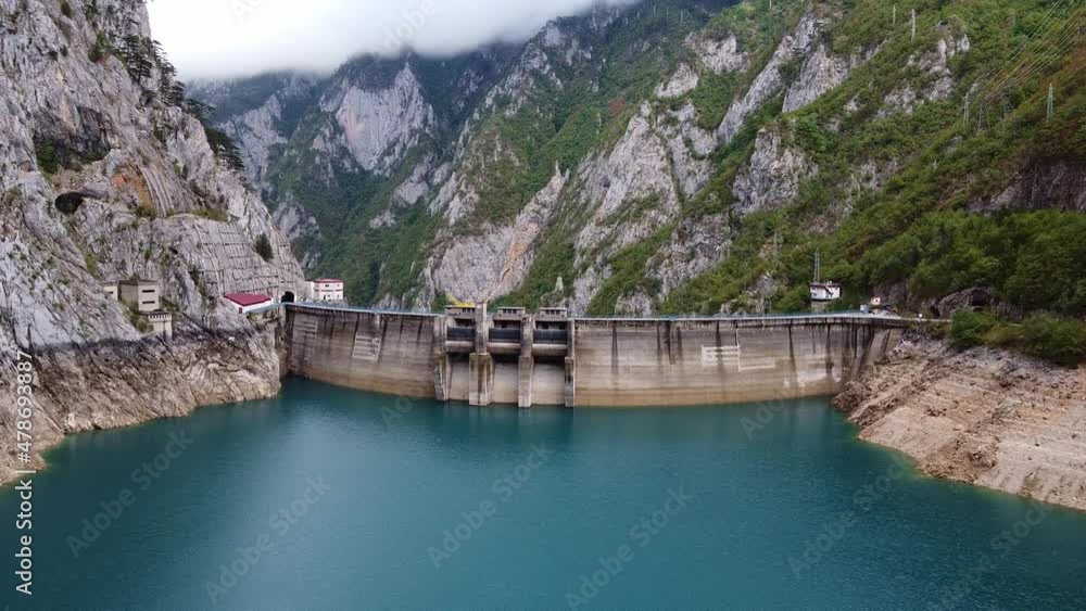 Drone view of water dam high in mountains. The mountain tops covered with clouds. Aerial view of Mratinje Dam (Piva Dam) in Montenegro. Drone view of water dam high in mountains. The mountain tops covered with clouds. Aerial view of Mratinje Dam (Piva Dam) in Montenegro.