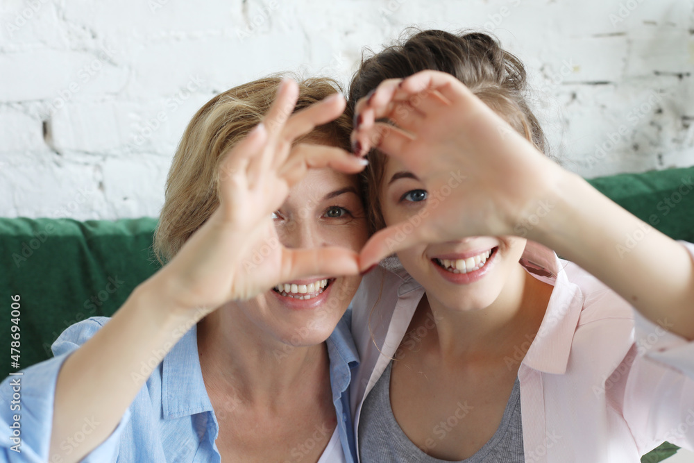 Mother and daughter love. Adult woman and young woman stacking hands in heart sign looking at camera.