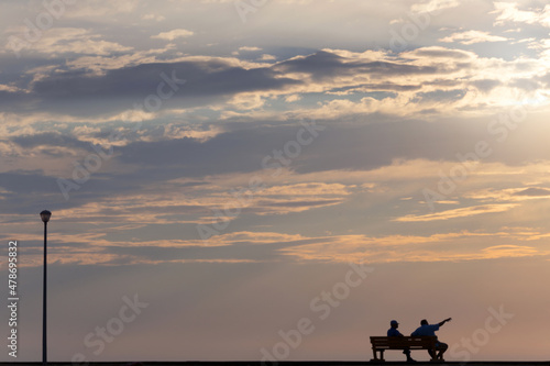 Two people sitting on a street bench and watching the dramatic sunset
