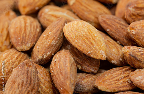 Close-up photo of almonds. Almond in the foreground to the right in selective focus. There are salt crystals on the roasted almonds.
