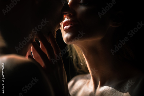 Sensual couple in the tender passion. Close up portrait of woman embracing and going to kiss man. Loving couple kissing over black background. Sexy lips.