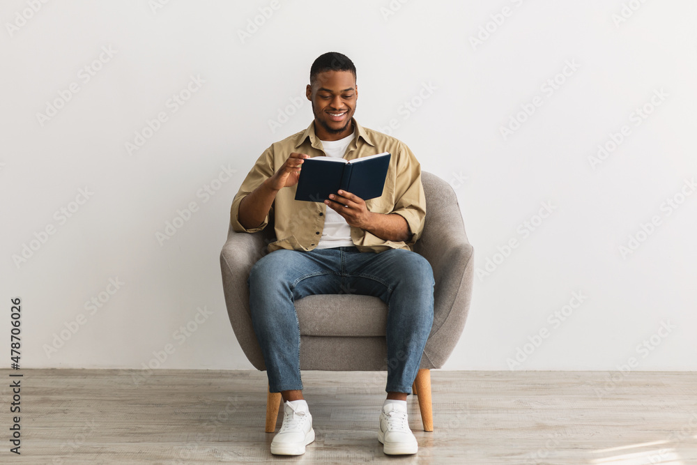 Black Man Reading Book Sitting In Armchair On Gray Background Black Man Reading Book Sitting In Armchair On Gray Background