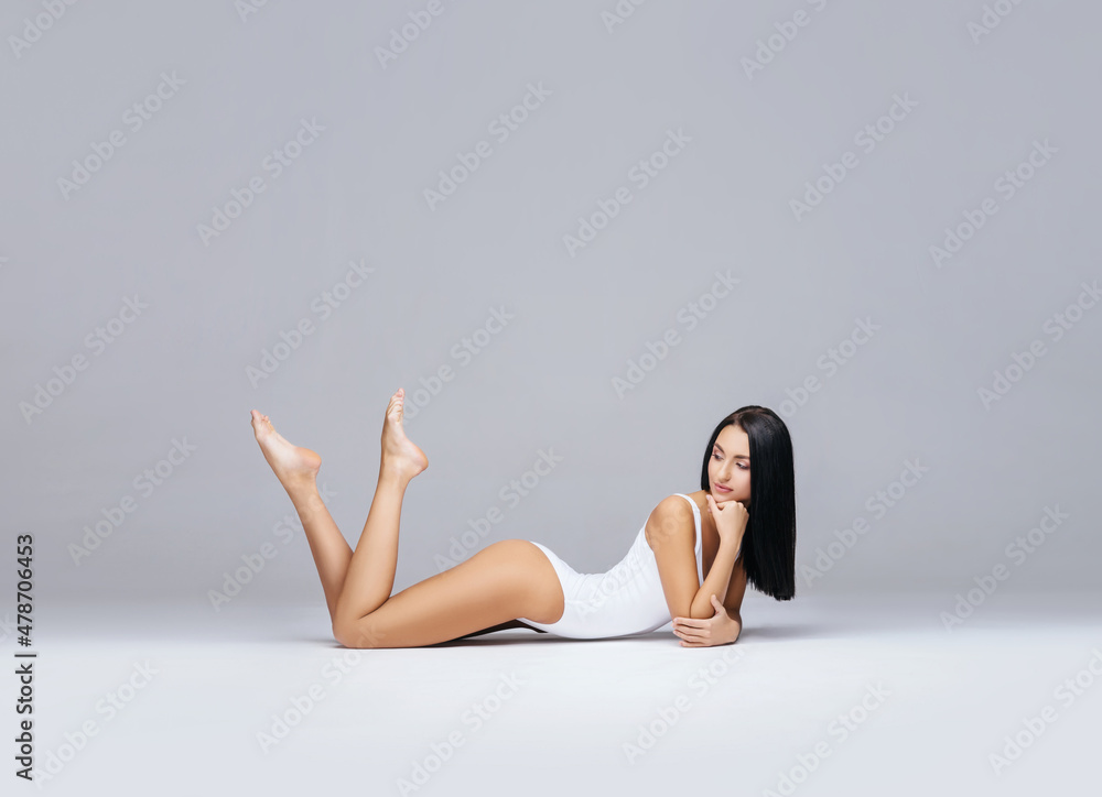Fototapeta premium Attractive and slender brunette girl in white underwear posing in studio. Healthy lifestyle, sport and body care concept.