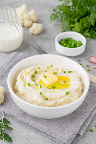 Cauliflower puree with butter and green onions in a white bowl on a gray concrete background. Healthy food. Copy space.