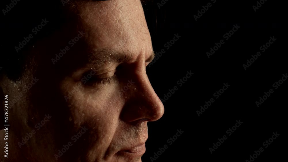 CLOSE UP: Face of sweating man wiped his wet forehead by hand on a black background CLOSE UP: Face of sweating man wiped his wet forehead by hand on a black background