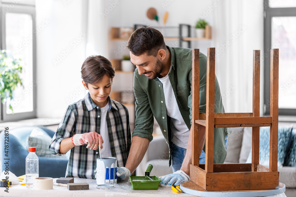 repair, diy and home improvement concept - father and son in protective gloves stirring grey color paint in can for painting old wooden table at home repair, diy and home improvement concept - father and son in protective gloves stirring grey color paint in can for painting old wooden table at home