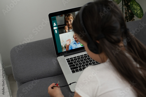Back view of young girl sit at home, talk have online video call lesson with teacher or tutor, teenage schoolgirl engaged in webcam conversation, study distant use web conference app on laptop
